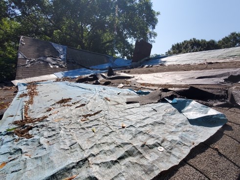 A roof with tarping and missing shingles.