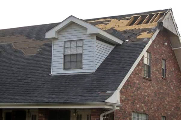 A home with severe roof damage. Portions of the roof's frame are exposed with many shingles missing.