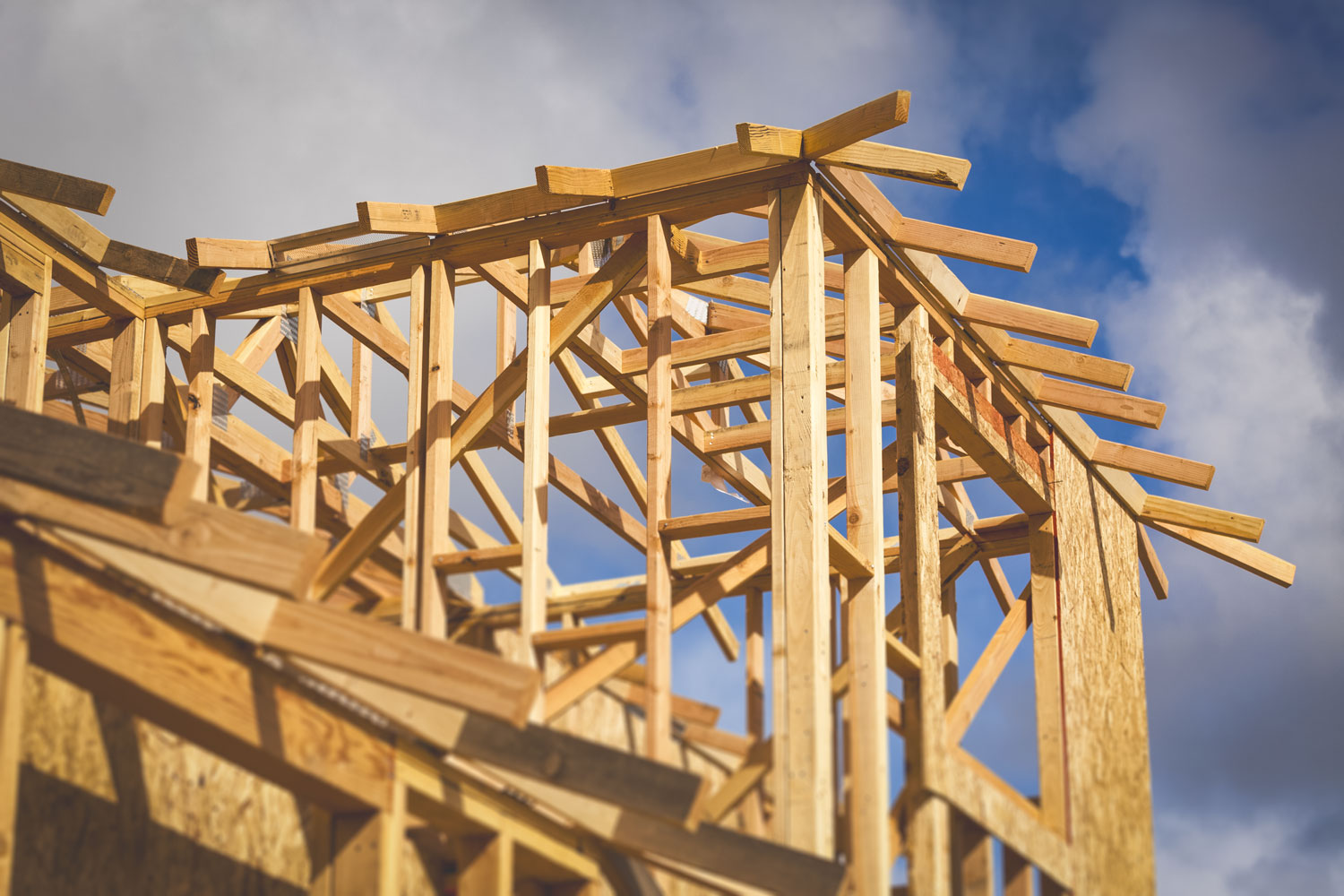 A home under construction with a frame in the foreground against a blue sky with clouds.