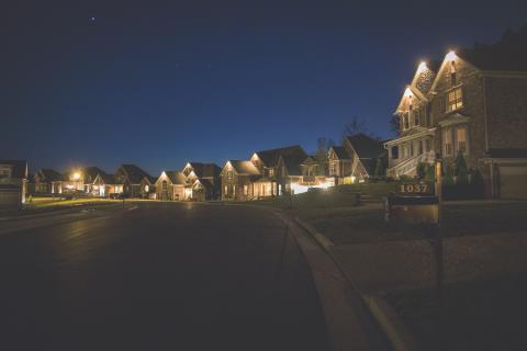 A neighborhood of single family homes at night. The homes are barely visible with porch lights providing bare illumination.